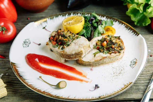 Restaurant dish with vegetable decor on a wooden background. Sea fish fried on a plate with sauce.