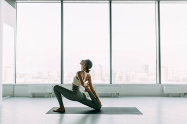  Stretching in the white room by the window. Beautiful girl athlete on the Mat. Flexibility exercises on a light background.