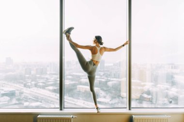  Stretching in the white room by the window. Beautiful girl athlete on the Mat. Flexibility exercises on a light background.