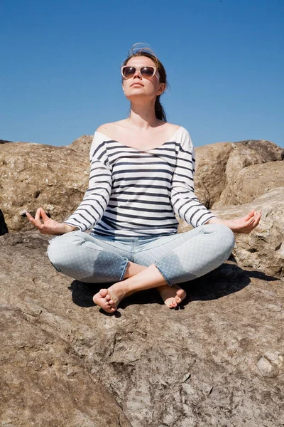 Ung attraktiv kvinna mediterar på klipporna mot himlen — Stockfoto