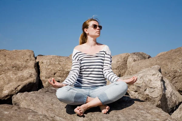 Ung attraktiv kvinna mediterar på klipporna mot himlen — Stockfoto