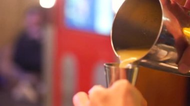 Barmen ölçü kabıyla bardağa portakal suyu dolduruyor.