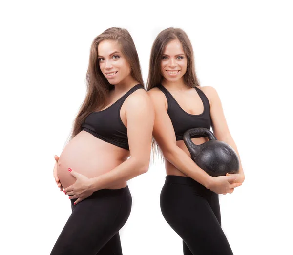 Una mujer embarazada con su hermana gemela. La hermana sostiene un peso de hierro fundido en sus manos. Sobre un fondo blanco . —  Fotos de Stock