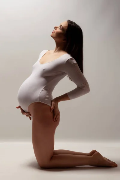 Gri Arka Planda Beyaz Bir Elbise Giymiş Hamile Bir Kadın — Stok fotoğraf