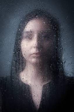 Siyah elbiseli ince esmer bir kız gri bir arka planda duruyor..