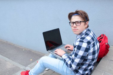 Oğlum genç (öğrenci veya öğrenci) merdivenlerde, gözlük, bir gömlek, gülümseyen, kırmızı sırt çantası içinde bilgisayar, çalışma oturuyor.