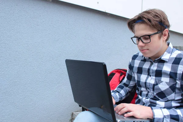 Oğlum genç (öğrenci veya öğrenci) merdivenlerde, gözlük, bir gömlek, gülümseyen, kırmızı sırt çantası içinde bilgisayar, çalışma oturuyor.