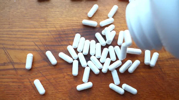 White capsules (medicines), tablets or vitamins scattered on a wooden table.
