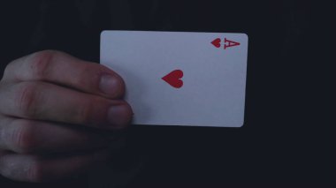 Bir iş adamı veya sihirbaz bir oyun kartı (kupa ASI), takım elbiseli, siyah bir arka plan tutar.
