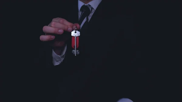 Businessman in suit holding keys in hands, black background.