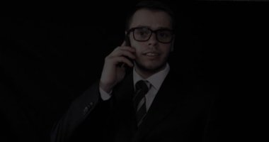 Bir takım elbise, siyah arka planda telefonda konuşurken gözlük, yakışıklı genç işadamı.