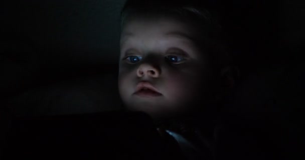 可爱的小孩在黑暗的房间里用智能手机看卡通片 蓝光的危险损害了他的眼睛 英俊的小男孩会患上与年龄有关的黄斑变性蓝光 — 图库视频影像