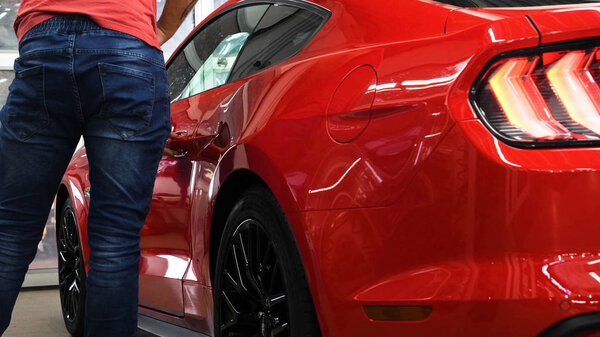 A man in the garage (car service) Checks the  red sport car alarm and then goes off (comes in) turning off (turning on) the lights behind him. Concept of: Auto garage, Security.