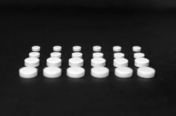 Tabletter fodrad i rader på en svart bakgrund, olika storlek, närbild — Stockfoto