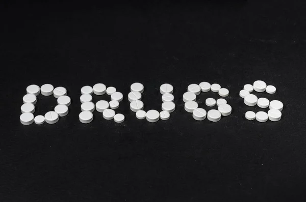 Das Wort "Drogen" ist aus Pillen auf dunklem Hintergrund ausgebreitet — Stockfoto