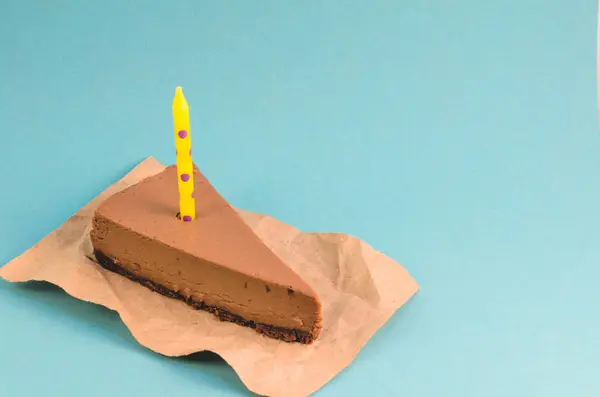 青い背景に黄色のキャンドルとチョコレートのチーズケーキの部分をクローズ アップ — ストック写真