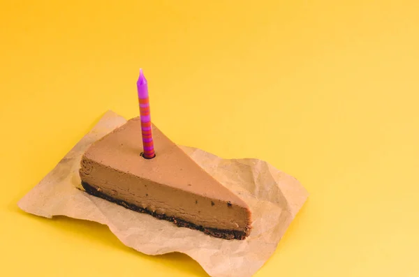 黄色の背景にライラックの蝋燭とチョコレートのチーズケーキの部分をクローズ アップ — ストック写真