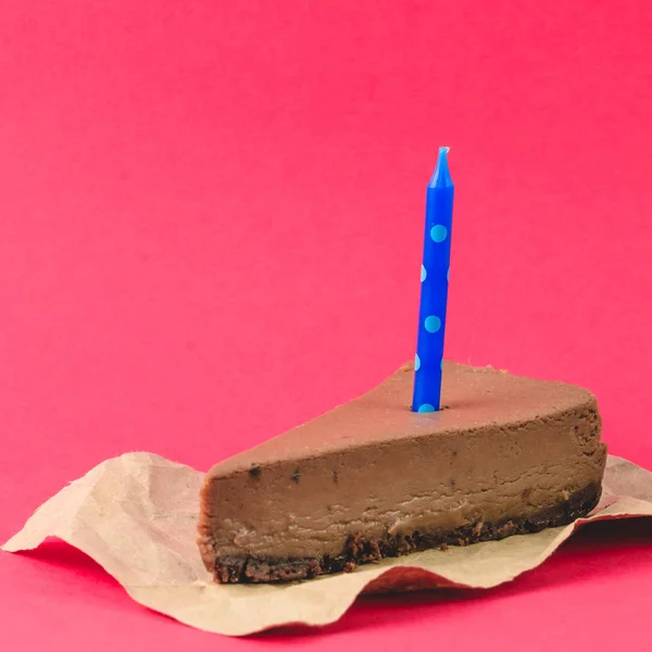 赤の背景に青いキャンドル チョコレート チーズケーキの部分をクローズ アップ — ストック写真