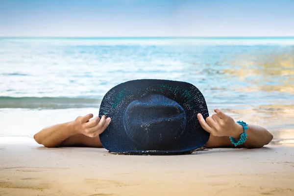 Νεαρή γυναίκα με το καπέλο βρίσκεται στη λευκή άμμο στην παραλία. Γαλάζια θάλασσα — Φωτογραφία Αρχείου