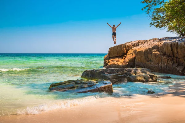 Der glückliche junge Mann springt von der Klippe ins Meer lizenzfreie Stockbilder