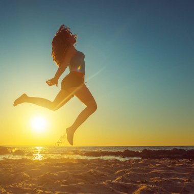 Mutlu kadın güzel sarı günbatımı karşı sahilde atlama