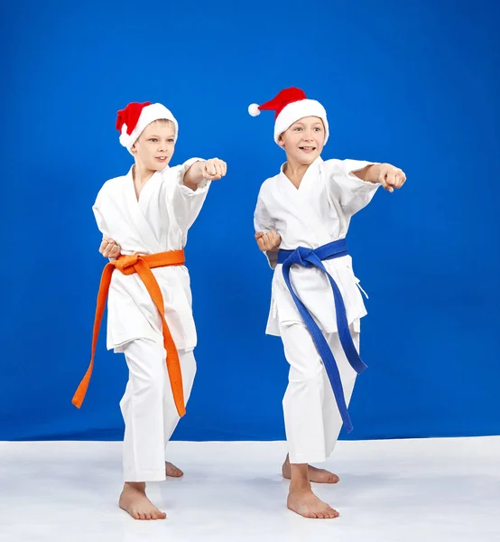 Two boys in caps of Santa Claus hit a punch arm in the rack of karate — Stock Photo, Image