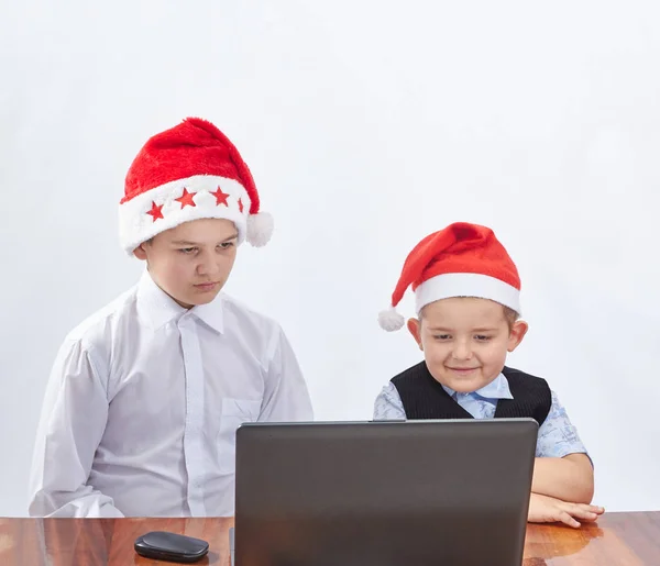 Fröhliche Kinder schauen auf einem Laptop in der Mütze des Weihnachtsmannes zu — Stockfoto