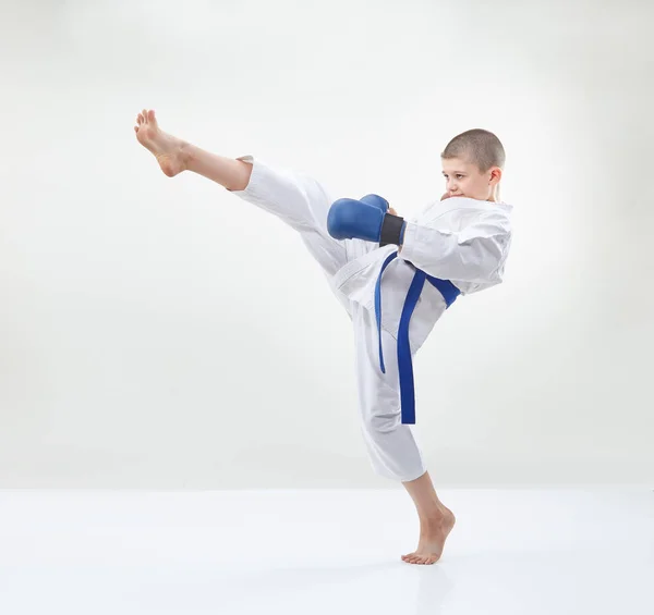 Chlapec v překrytí karategi a modré na rukou bije kop nohou — Stock fotografie