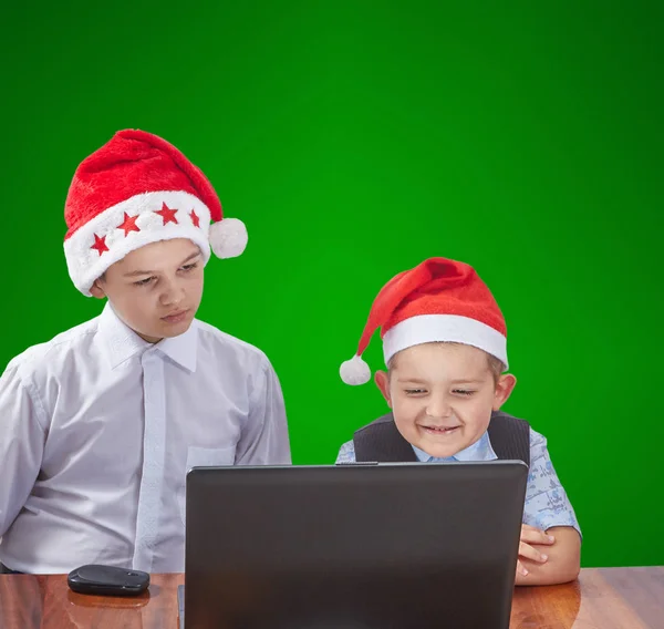 En un fondo verde chicos en gorras de Santa Claus mirando a un ordenador portátil — Foto de Stock