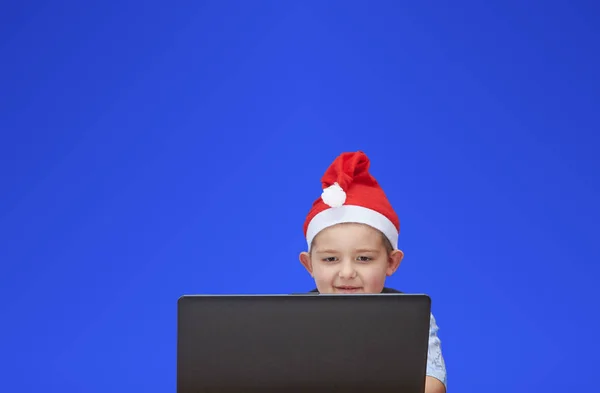 Auf blauem Hintergrund ein Junge, der auf einen Laptop blickt — Stockfoto