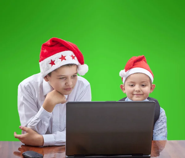 In Mützen von Weihnachtsmännern blicken Kinder interessiert auf einen Laptop — Stockfoto