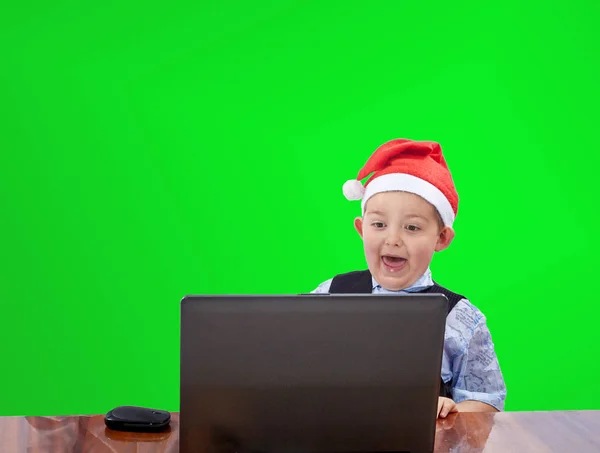 Fröhliches Kind mit Weihnachtsmannmütze und Blick auf einen Laptop — Stockfoto