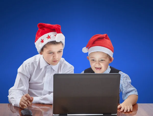 Auf blauem Hintergrund beobachten Kinder auf einem Laptop und sitzen an einem Tisch — Stockfoto