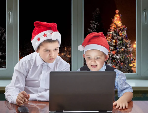 Los hermanos están mirando un portátil en el fondo del árbol de Navidad decorado fuera de la ventana — Foto de Stock