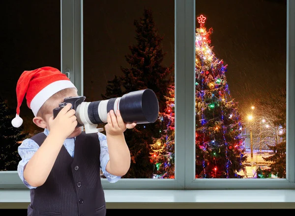 Il ragazzo sta fotografando sulla macchina fotografica su uno sfondo decorato albero di Natale fuori dalla finestra — Foto Stock