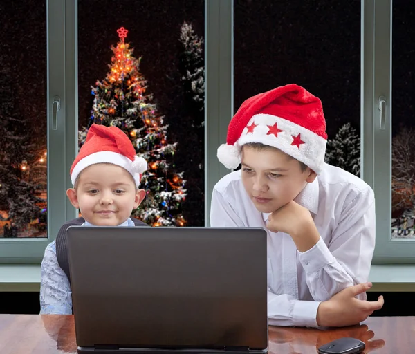 En el fondo del árbol de Navidad fuera de la ventana dos hermanos están mirando un portátil — Foto de Stock