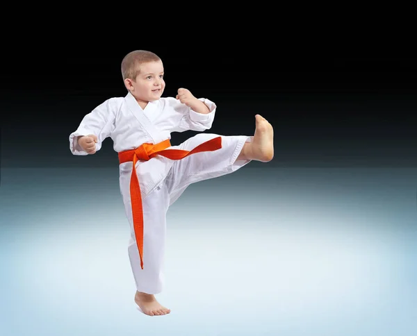 Chłopiec w karategi uderza kick na gradientowym tle — Zdjęcie stockowe