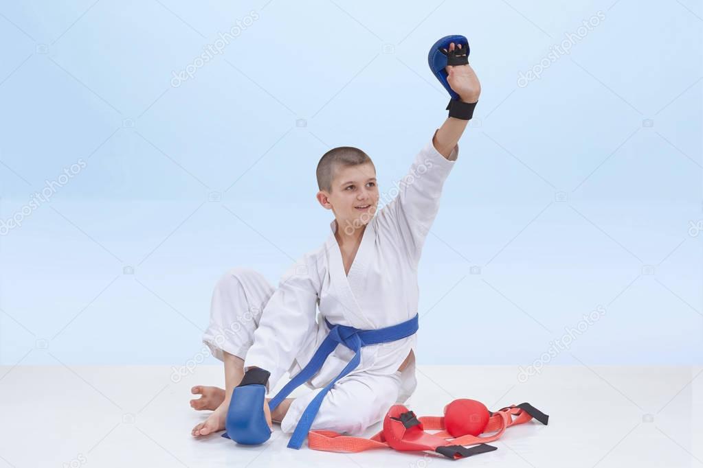 Karate boy with a blue belt is sitting near karate outfit