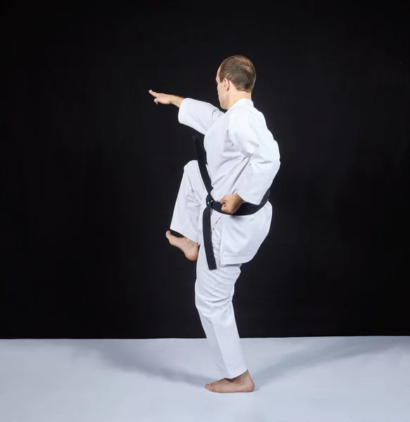 På svart bakgrund slår en karate idrottare med ett knä — Stockfoto