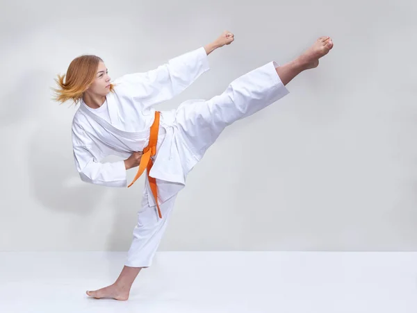 With an orange belt the girl beats a kick — Stock Photo, Image