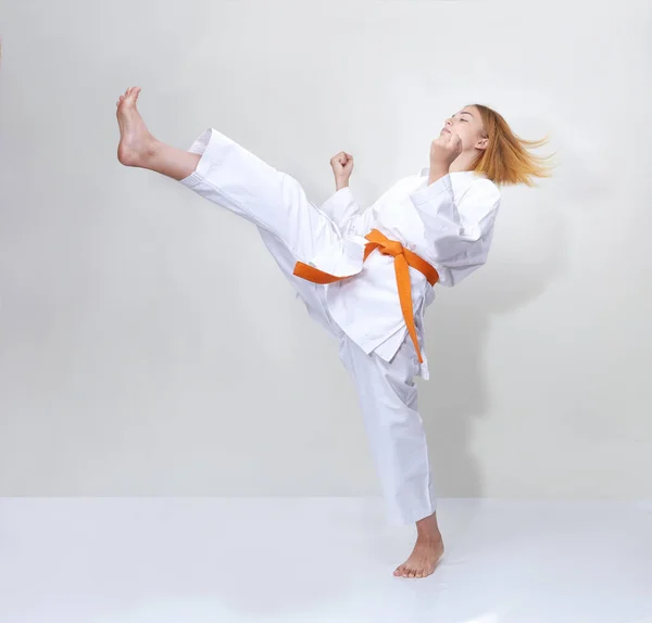 Sportovkyně s oranžovým pásem bije kop na šedém pozadí — Stock fotografie