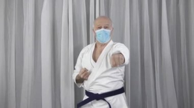 Tıbbi maskeli yaşlı bir atlet kolları yumrukluyor ve blokları eğitiyor.