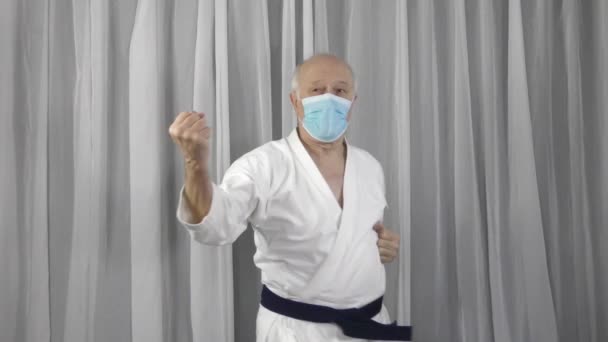 Karatégiban Orvosi Maszkban Egy Öreg Sportoló Blokkokat Ütéseket Gyakorol — Stock videók