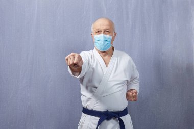Tıbbi maskeli ve mavi kemerli yaşlı bir sporcu yumruğu yener.