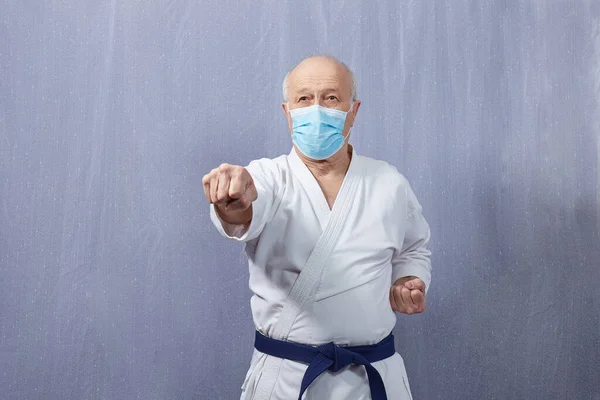 Old man athlete in a medical mask and with a blue belt beats a punch