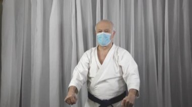 Karategi ve tıbbi maskeli yaşlı bir erkek sporcu elleriyle blokları eğitiyor.