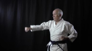 Yaşlı sporcu siyah arka planda blok ve yumruk atıyor.