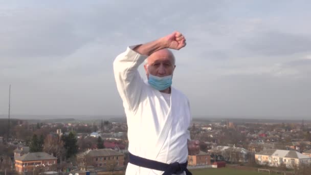 一位戴着医疗面具的老运动员用手在城市的背景上做着方块 — 图库视频影像