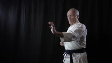 Siyah arka planda, yaşlı bir erkek atlet yumruk ve blokları eğitiyor.