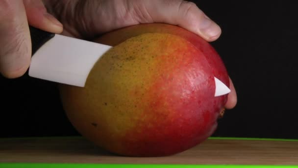 Mains coupant la mangue sur fond noir 